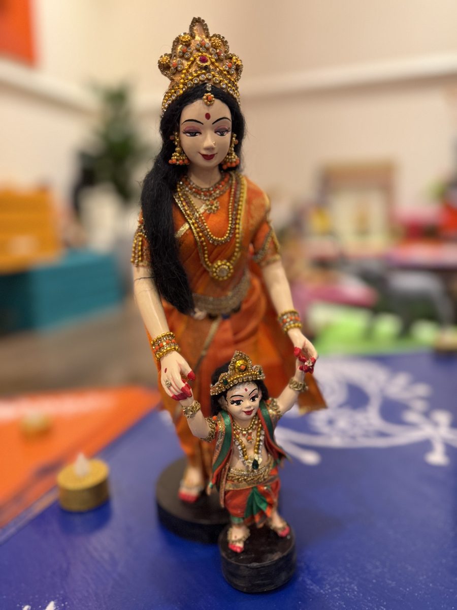 Golu doll of a Karthigai maiden in an orange sari holding the hands of baby Murugan as he takes his first steps