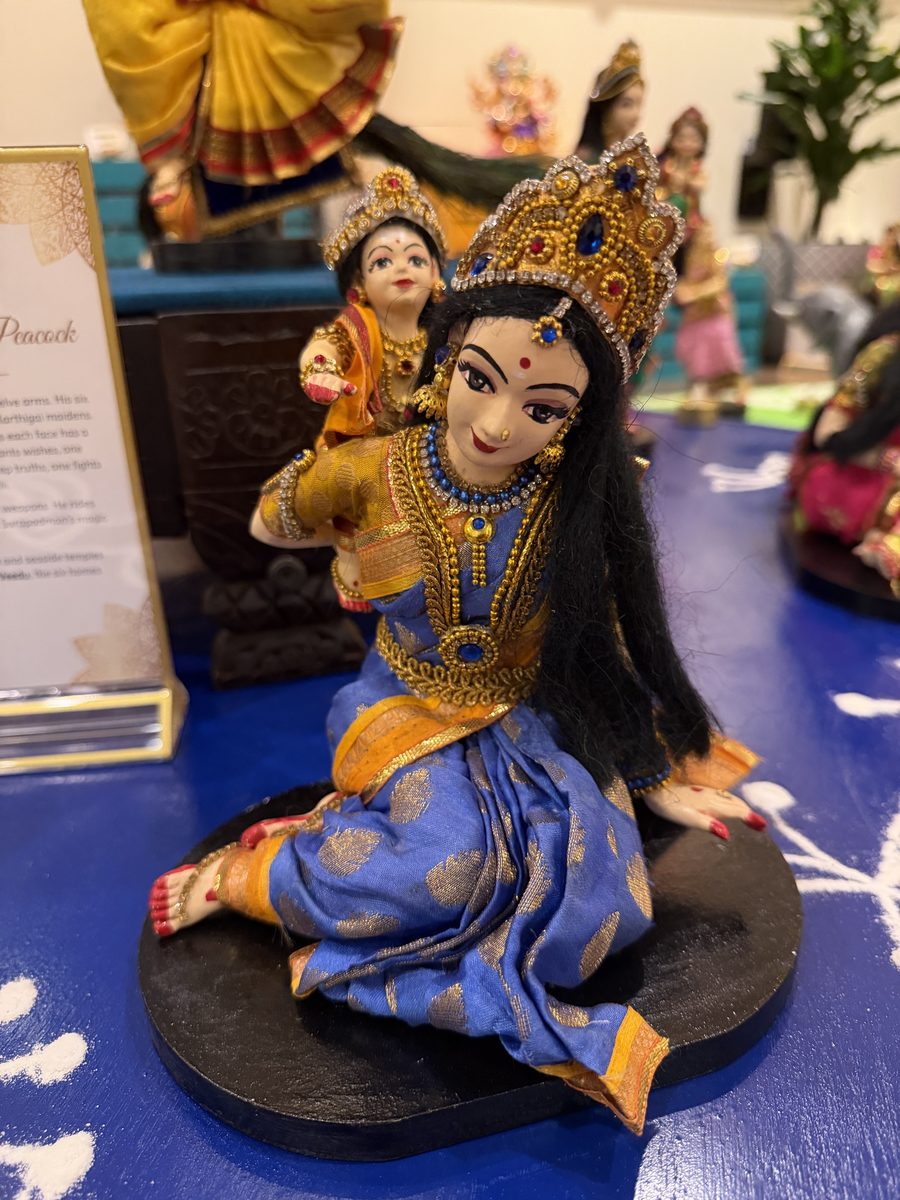 Golu doll of a Karthigai maiden in a blue sari, seated, carrying baby Murugan on her shoulder